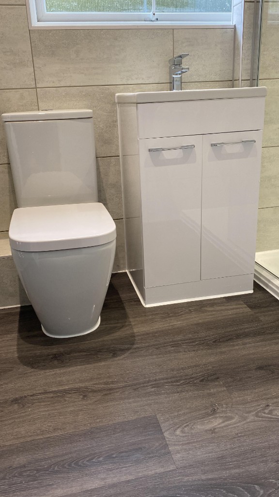 Professional white bathroom silicone around toilet and vanity unit on wood-effect flooring in Cardiff area renovation