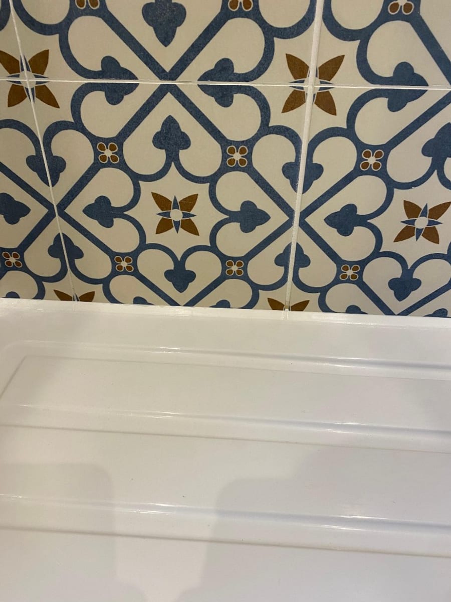 Clean, straight white silicone seal between a white shower tray and blue and cream patterned feature tiles after a professional reseal in South Wales