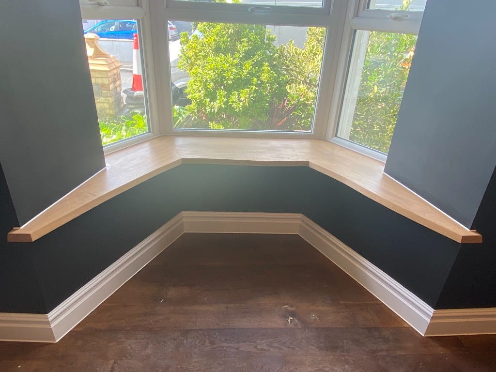 Bay window with oak window board against dark painted walls and white skirting neatly sealed in South Wales