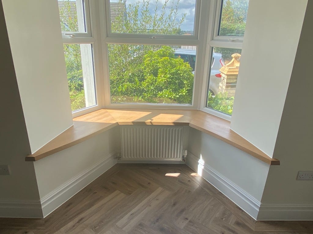 Bay window with oak window board and white skirting neatly sealed to the walls and herringbone floor in a South Wales home