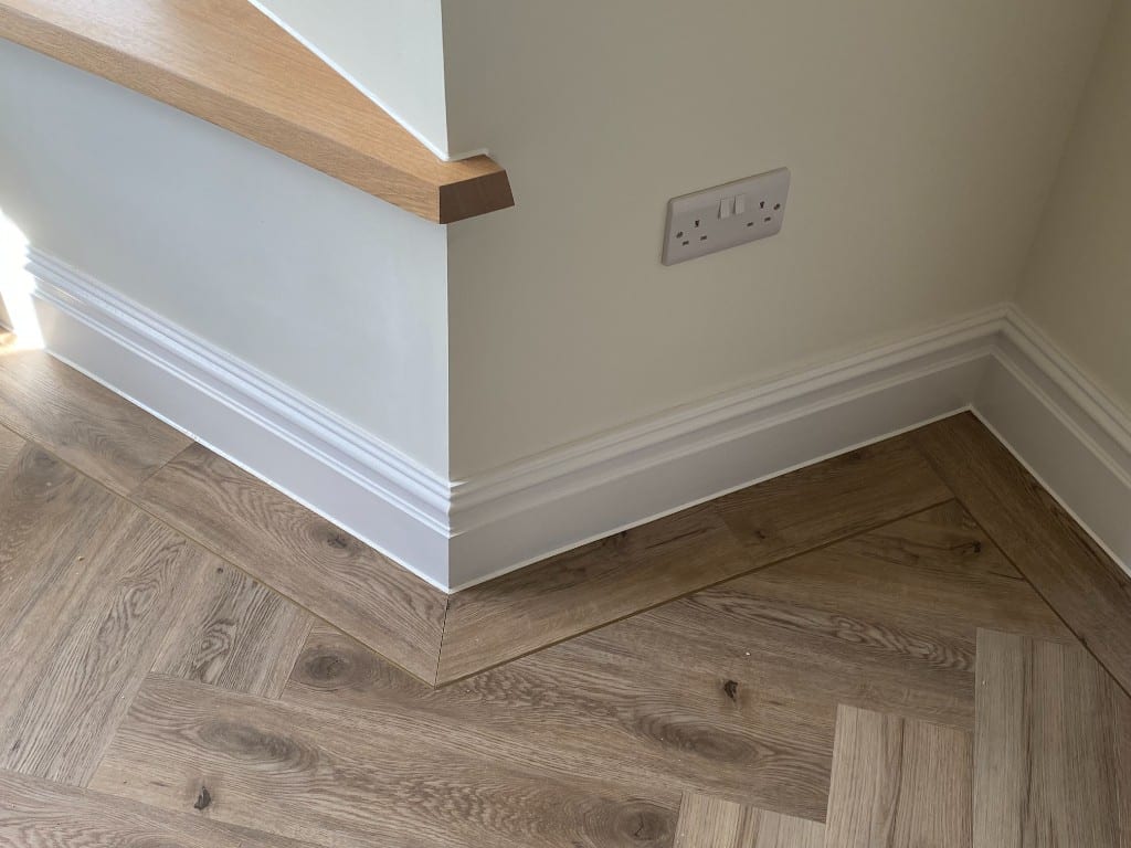 Close-up of white skirting board neatly sealed to the wall and herringbone floor at the corner of a bay window in South Wales